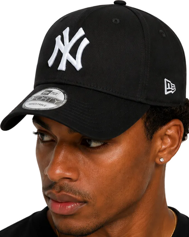 A close-up of a man wearing a black New Era 9FIFTY baseball cap with a white embroidered New York Yankees logo on the front and a silver visor sticker.