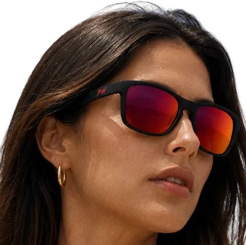 a woman wearing black sunglasses with vibrant red mirrored lenses, photographed outdoors against a blue sky.