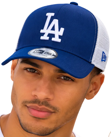 A close-up of a man wearing a blue and white Los Angeles Dodgers trucker hat with a New Era 9FIFTY sticker on the brim, set against a bright blue sky background.
