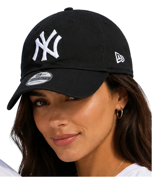 lady wearing black New York Yankees baseball caps with white embroidered logos, photographed against a clear light blue sky.