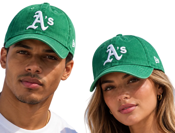 Two models wearing green Oakland Athletics baseball caps with white 'A's' logos, photographed against a clear blue sky.