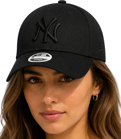 A close-up of a woman wearing a black New Era baseball cap with an embroidered black New York Yankees logo on the front. The cap features a curved brim, a white sticker on the brim, and a small black logo on the side, set against a plain white background.